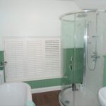 Green bathroom with low window and white shutters
